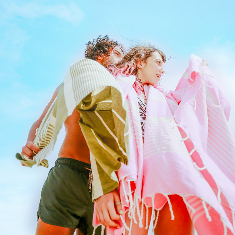 ein Paar mit einem rosa und einem khakifarbenen XXL Strandtuch 