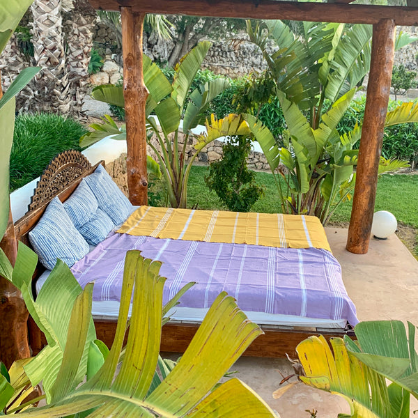 ein gelbes Strandtuch und eine hellgraue Fouta bedecken ein Bett im Freien