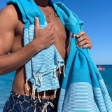 Mann mit aquablauem Strandtuch fouta auf den Schultern am Strand