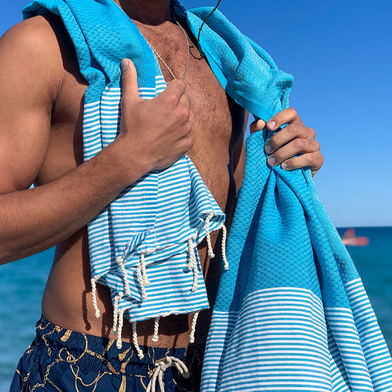 ein Mann am Strand mit blauem Strandtuch fouta auf den Schultern