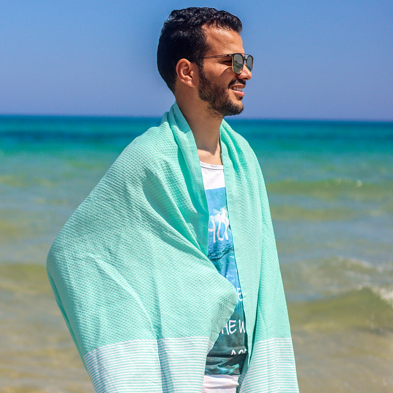 Mann am Strand mit aquablaues Strandtuch saunatuch auf den Schultern