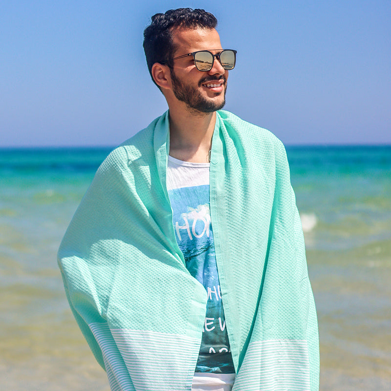 Mann mit Sonnenbrille am Strand mit aquablauem Strandtuch