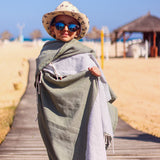 ein Kind mit Sonnenbrille und Hut, das ein braunes Strandtuch trägt