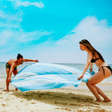 ein Paar am Strand das ein aquablaues Strandtuch hält