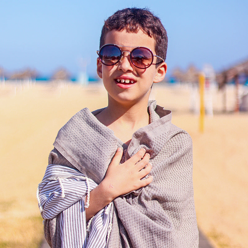 Kind mit Sonnenbrille eingewickelt in eine hellbraune strandtuch am Strand
