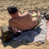 Mann am Strand der sich auf einem hellbraunen Hamamtuch räkelt