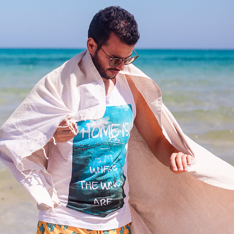 Mann mit einem beigen Strandtuch auf den Schultern am Strand