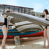Mädchen am Strand die ein platingraues Strandtuch fouta neben dem Boot halten