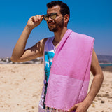 Mann mit Sonnenbrille am Strand mit rosa Hamamtuch auf der Schulter