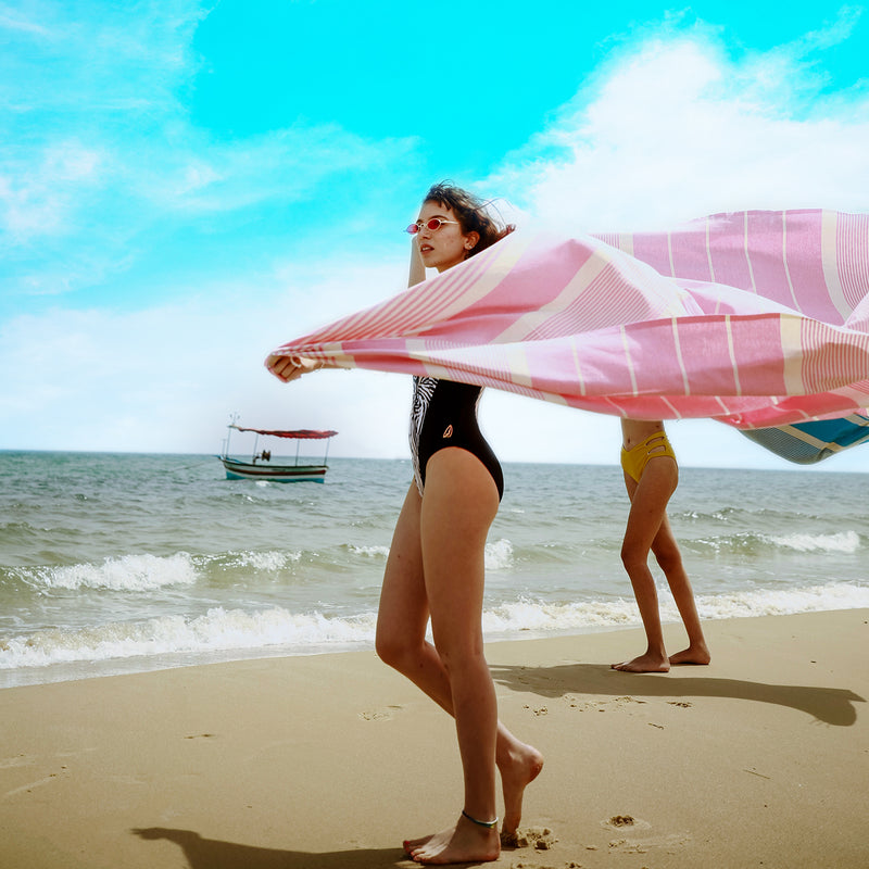  zwei Mädchen am Strand die ein rosa XXL Strandtuch fouta halten 