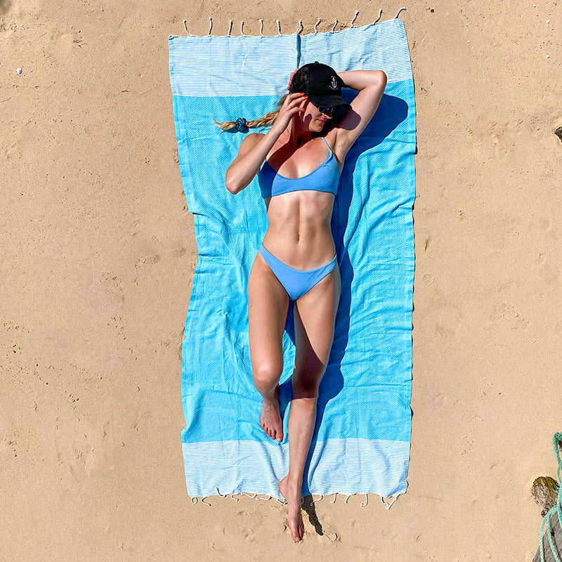 Mädchen im Bikini beim Sonnenbaden auf einem blauen Strandtuch fouta am Strand