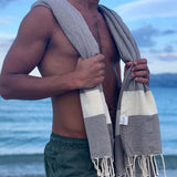Mann am Strand mit hellbraunem Strandtuch fouta auf den Schultern