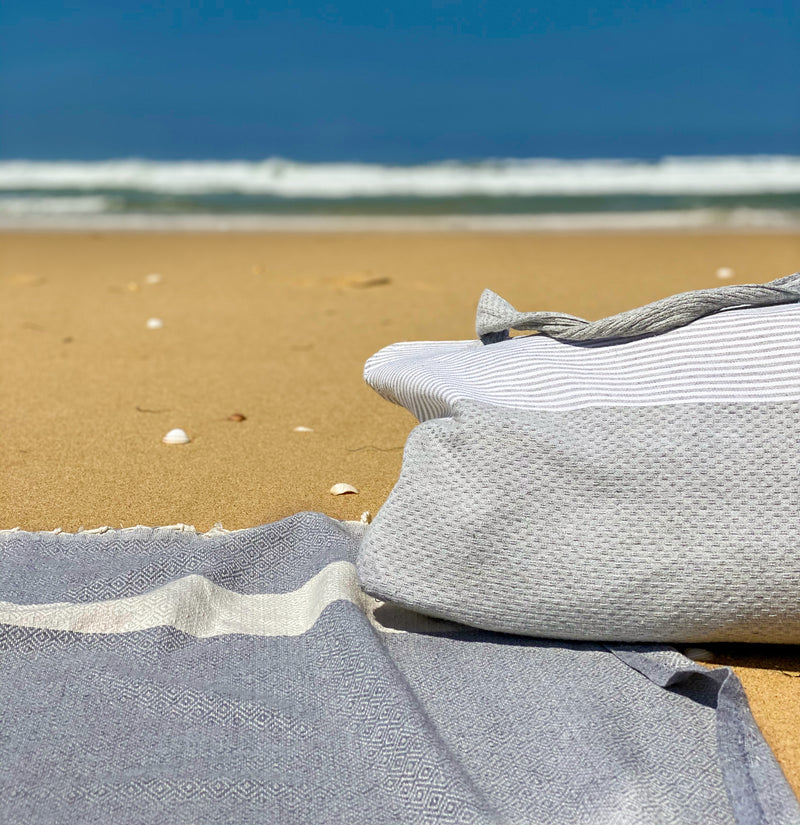 graues Strandtuch fouta und Strandtasche im Sand