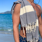 Mann am Strand mit dunkelblauem Strandtuch auf der Schulter