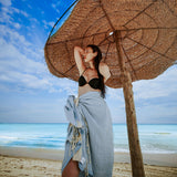 Mädchen im schwarzen Bikini mit blauer Saunatuch unter Sonnenschirm am Strand
