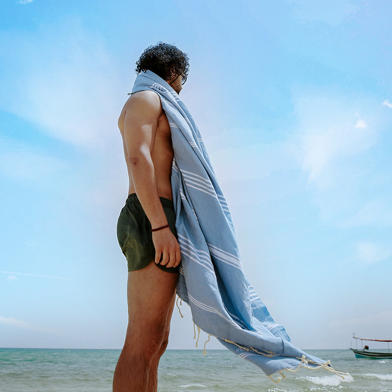 ein Mann am Strand mit jeansblauem Hamamtuch auf den Schultern