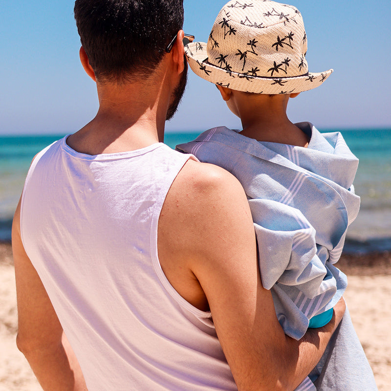 Vater hält seinen Sohn in hellblauer Hamamtuch Fouta am Strand