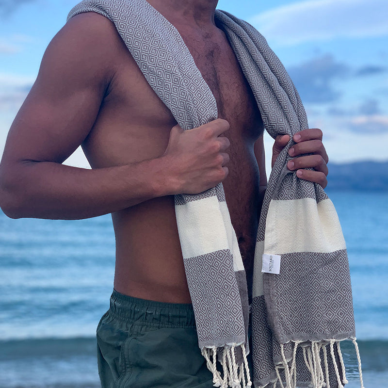 ein Mann am Strand mit braun Strandtuch fouta auf den Schultern