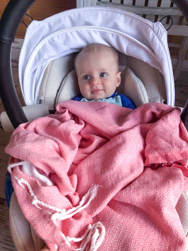 Baby im Kindersitz bedeckt mit einem rosa Hamamtuch 