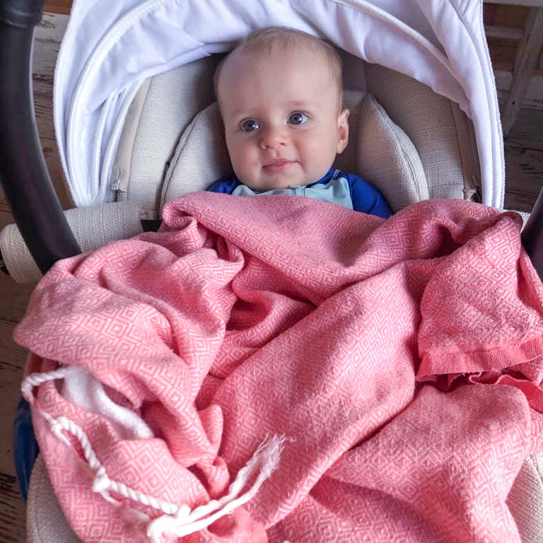 ein Baby in seiner Babyschale bedeckt mit rosa Fouta