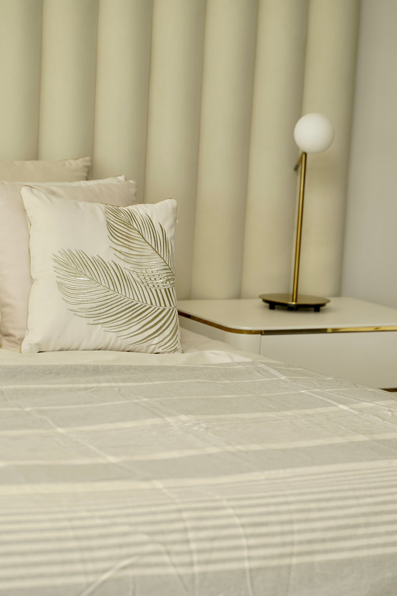 ein Bett mit einem pastellgrauen Bettüberwurf und weiß-goldenen Kissen